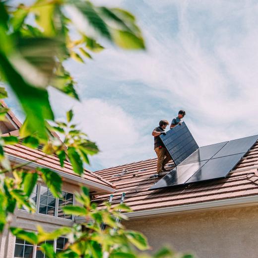 Zwei Männer installieren Solarmodule auf einem Hausdach.
