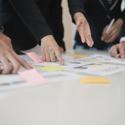 Ein Tisch mit Post-Its und bedruckten Blättern, auf die verschiedene Hände und Finger zeigen