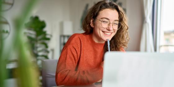 Eine junge Frau sitzt lächelnd vor ihrem Laptop