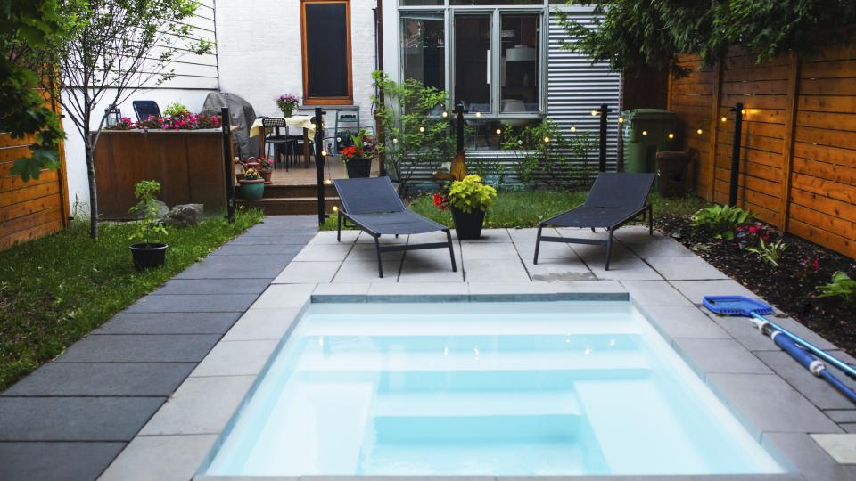 Kleiner Pool in einem Garten mit zwei Liegestühlen im Hintergrund.