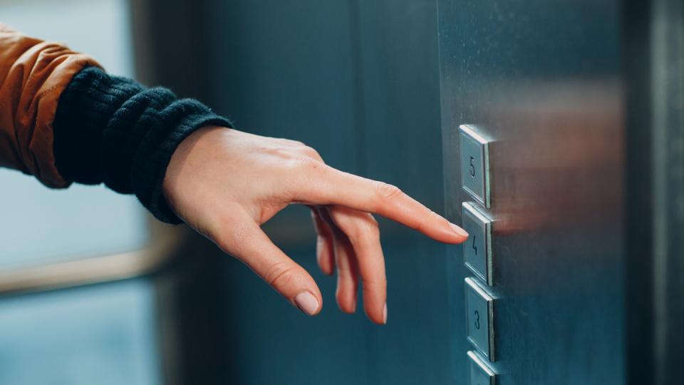 Ein Finger zeigt auf einen Etagenknopf eines Aufzuges.