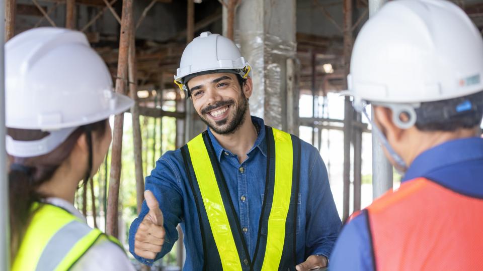 Arbeiter auf einer Baustelle zeigt den Daumen nach oben für andere Mitarbeiter.
