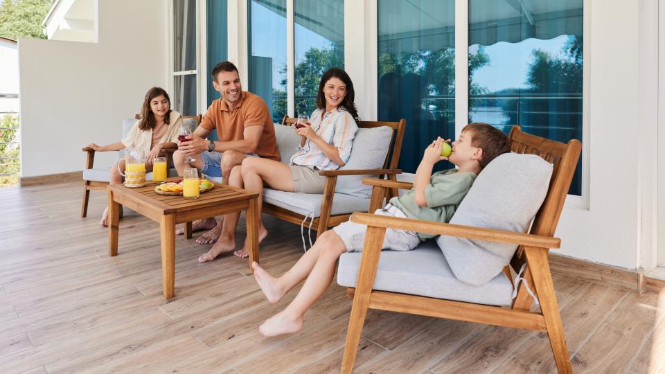 Eine Familie mit zwei Kindern sitzt auf einer Terrasse und trinkt Orangensaft.