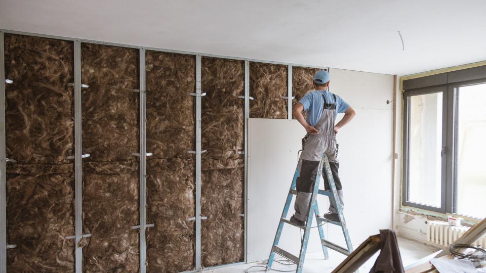 Mann steht auf einer Leiter vor einer Wand, die aufgebaut wird.