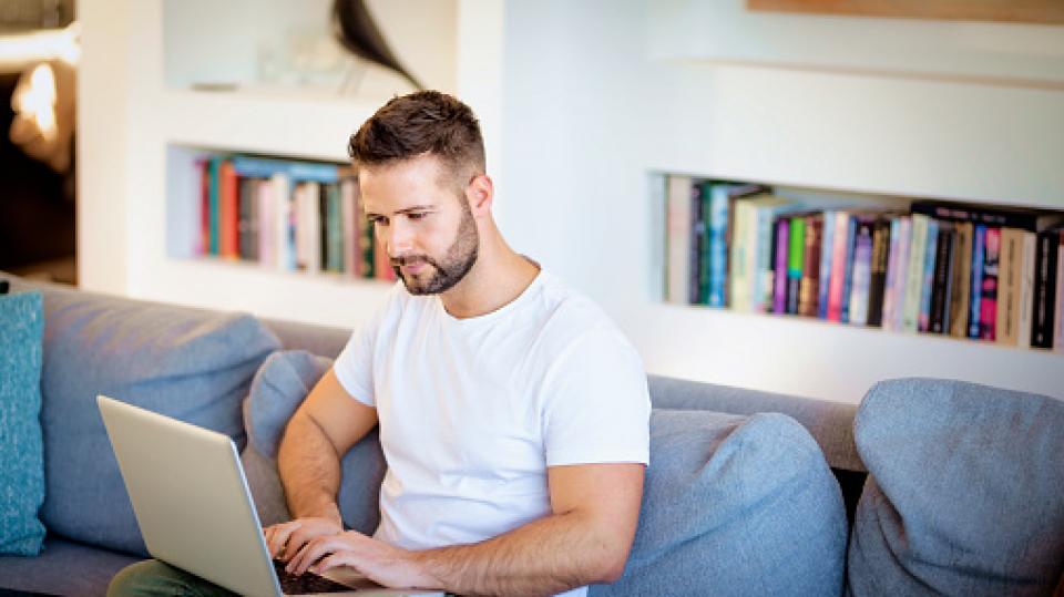Ein Mann mit Laptop sitzt auf der Couch.