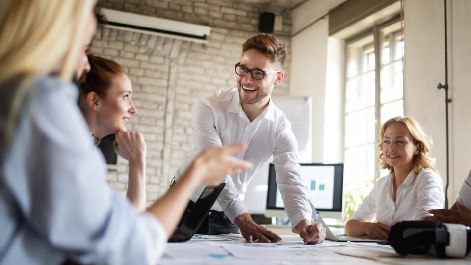 Vier Menschen sitzen an einem Tisch in einem Büro, in der Mitte liegt ein großes Dokument